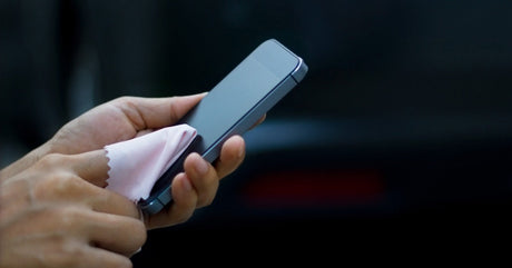 A person uses a cloth on their finger to wipe the screen of a black smartphone.