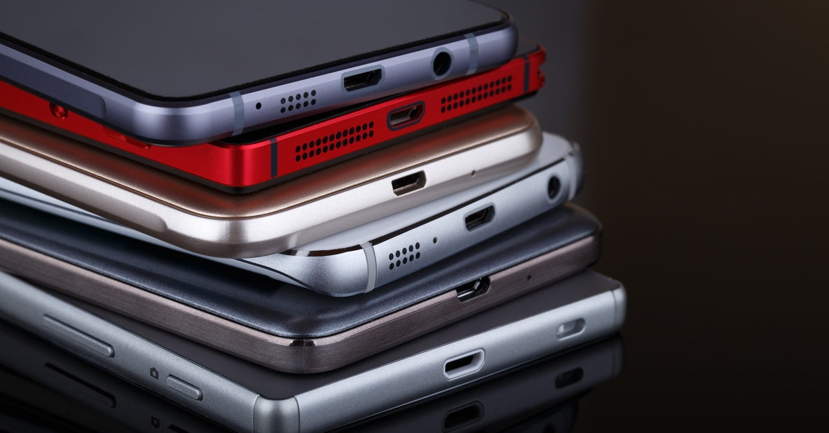 A stack of smartphones on top of each other. Each smartphone looks different and comes in varying colors.