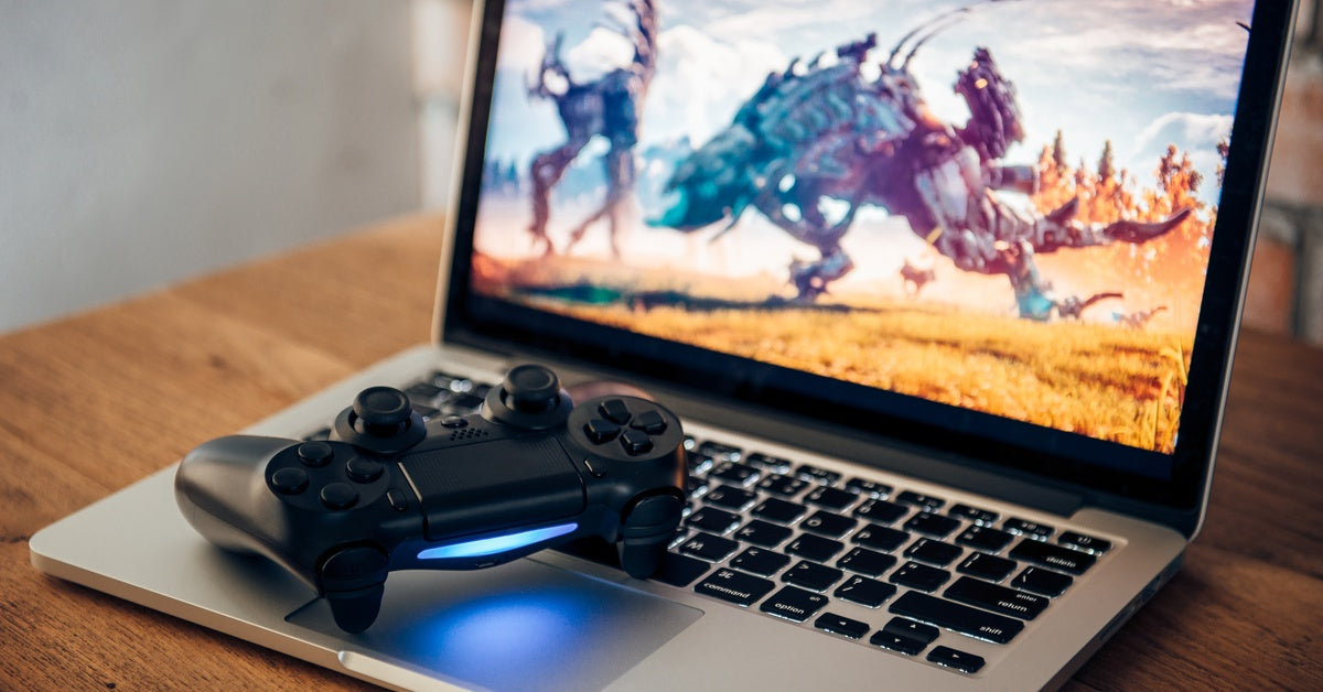 Laptop on wooden surface with PlayStation controller on keyboard, screen showing vivid game scene of futuristic battle.