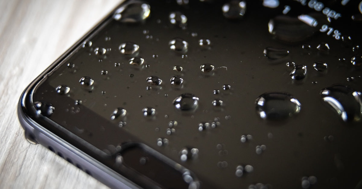A smartphone screen covered in scattered water droplets, resting on a light wood surface with 91% battery showing.