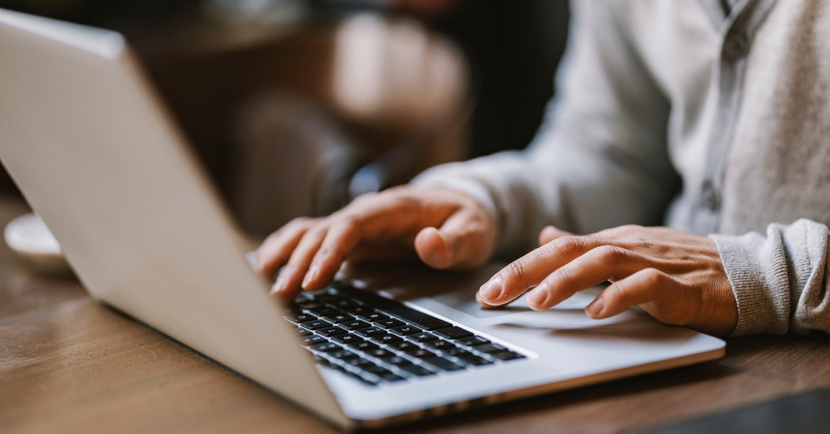 A close-up of someone using a MacBook laptop that is resting on a table. Their fingers hover over the keyboard and trackpad.