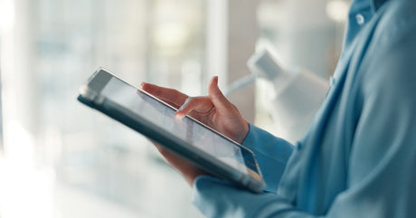 A close-up of someone holding a tablet in one hand and using their finger on the other hand to tap the screen.